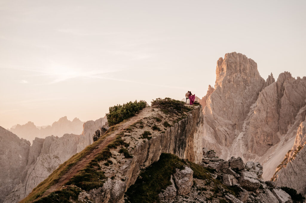 Couple standing on mountain cliff at sunset.