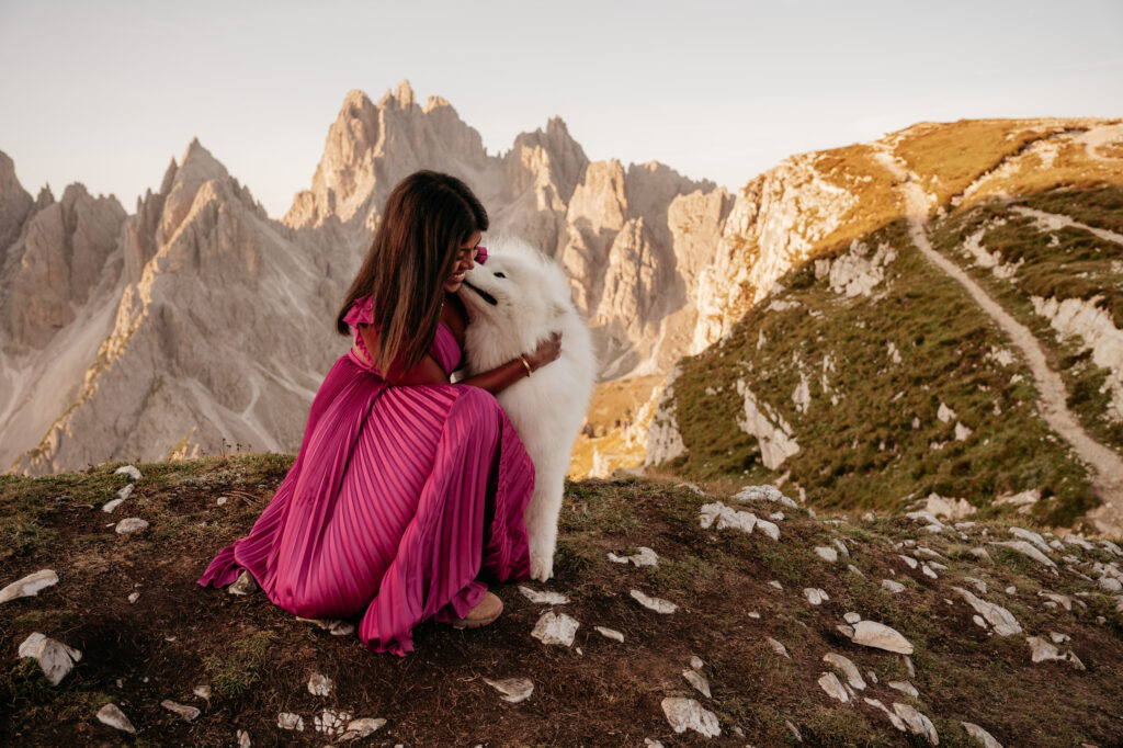 Woman in pink dress hugging fluffy dog mountains