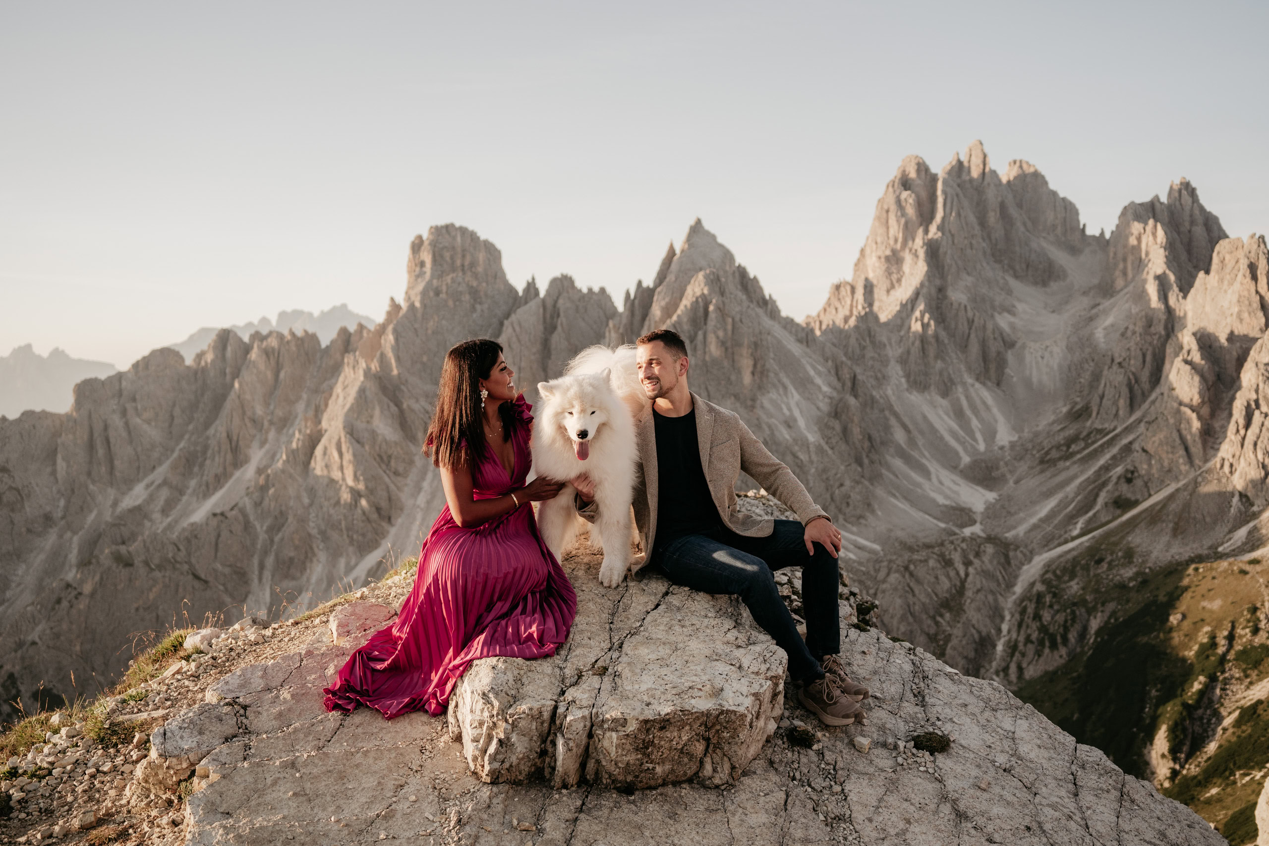 Couple with dog on mountain cliff at sunrise.