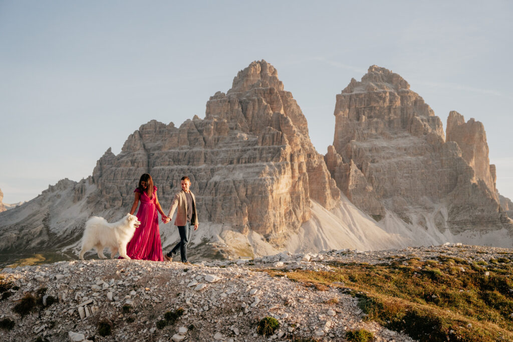 Couple with dog hiking near scenic mountain landscape.