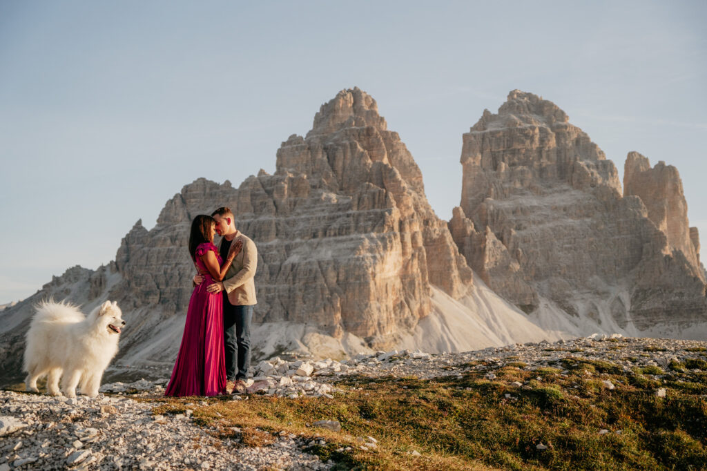 Couple embraces with dog in rugged mountain landscape.