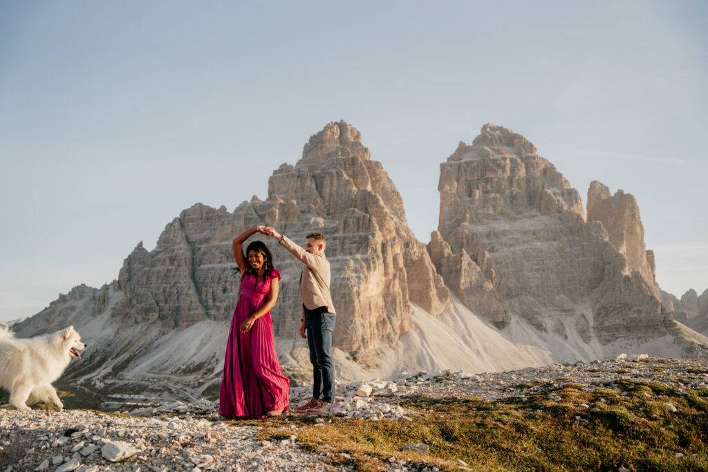 Couple dances with dog in mountain landscape.