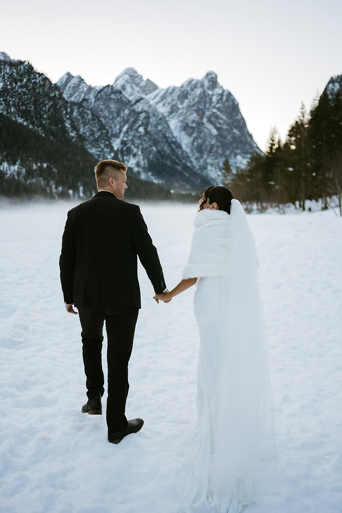 Couple holding hands in snowy mountain landscape.