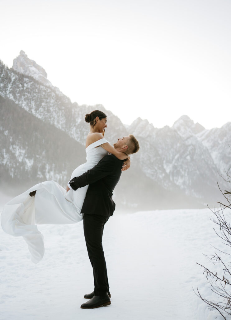 Couple embraces in snowy mountainous landscape.