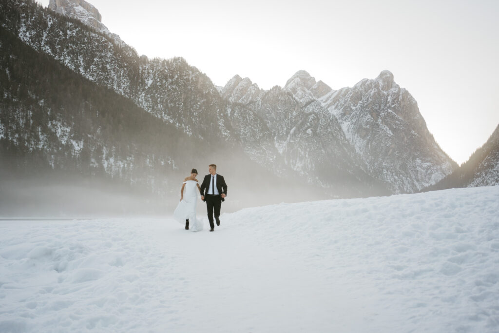 Couple walking on snowy path with mountains background.