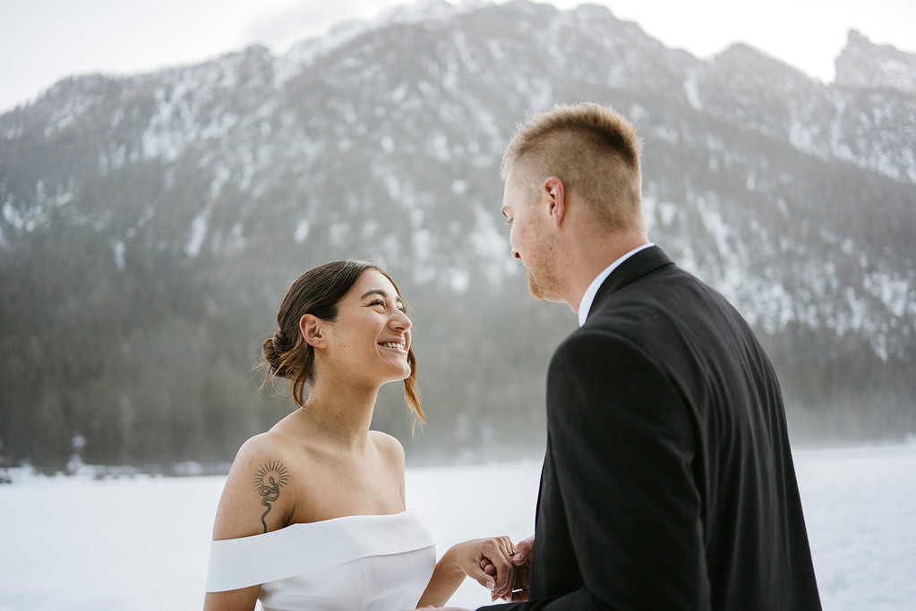 Wedding couple smiling in snowy mountain setting.