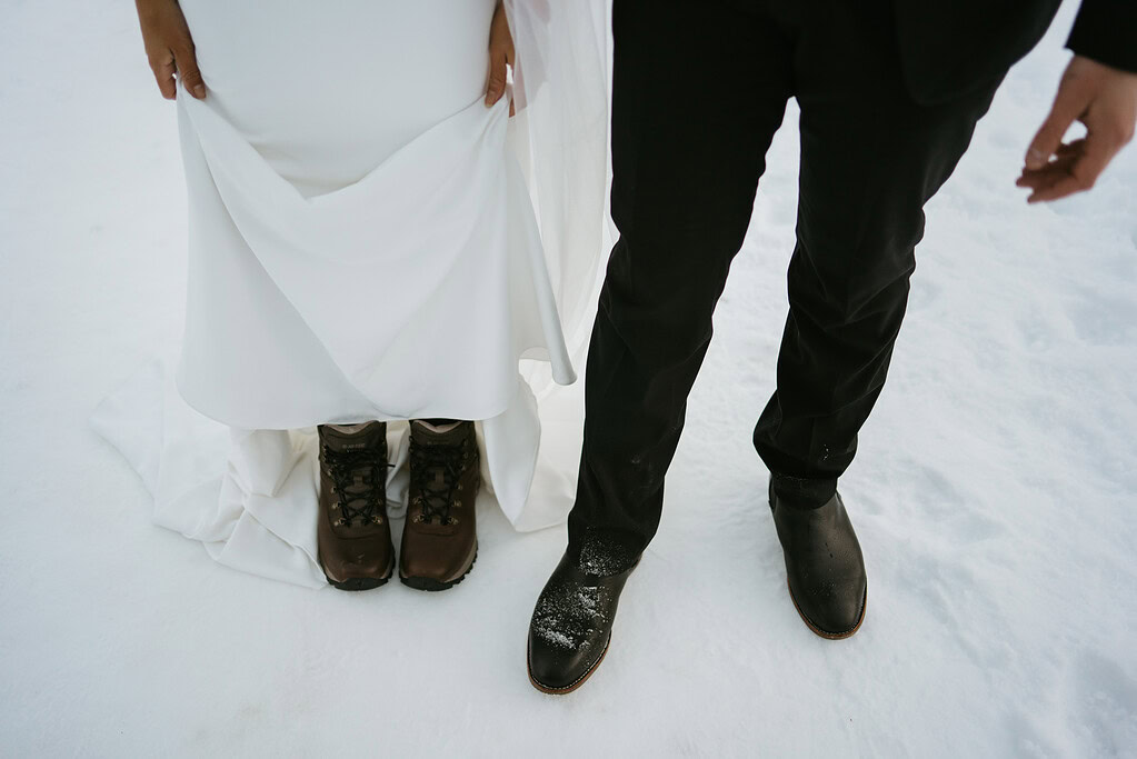 Bride and groom in snow, boots and dress shoes.