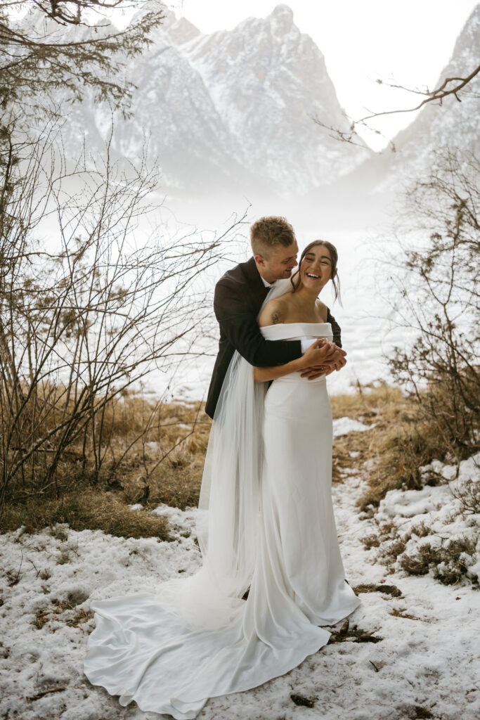 Bride and groom embracing in snowy mountain landscape.