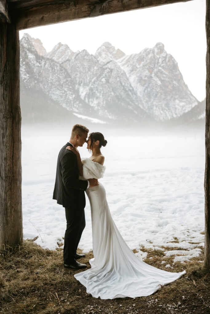 Bride and groom embrace by snowy mountain landscape.