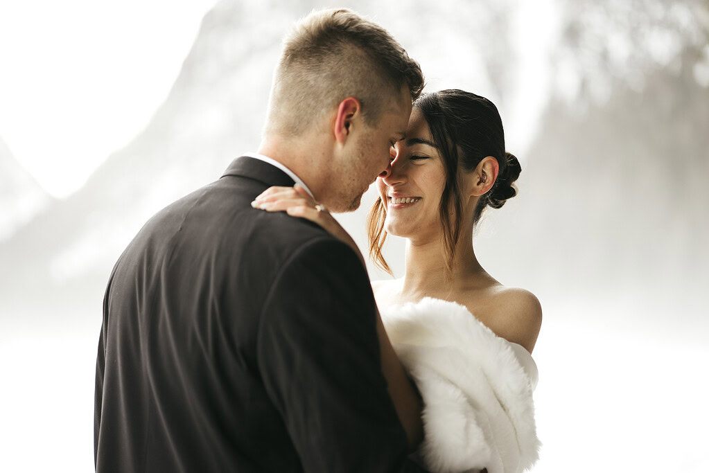 Bride and groom embrace in snowy backdrop.