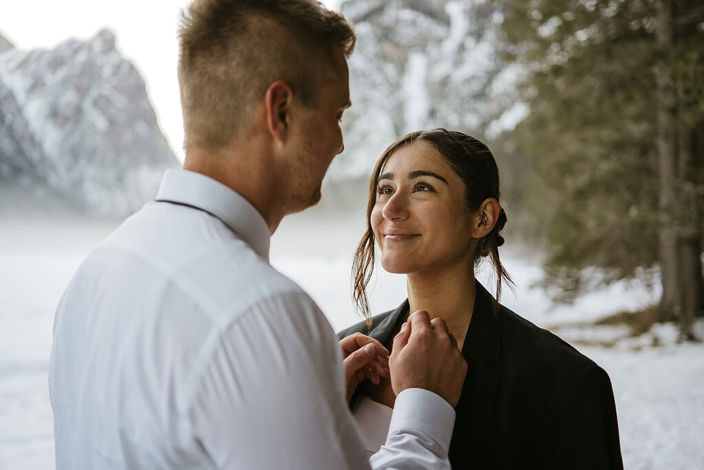 Couple smiling in snowy forest setting.