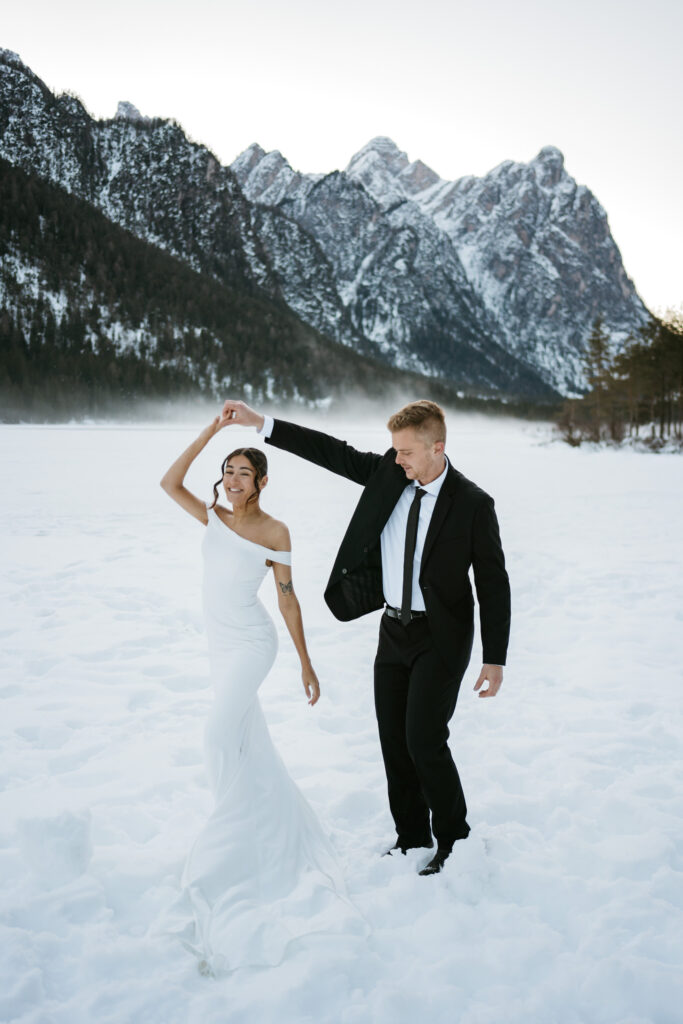 Bride and groom dancing in snowy mountain landscape