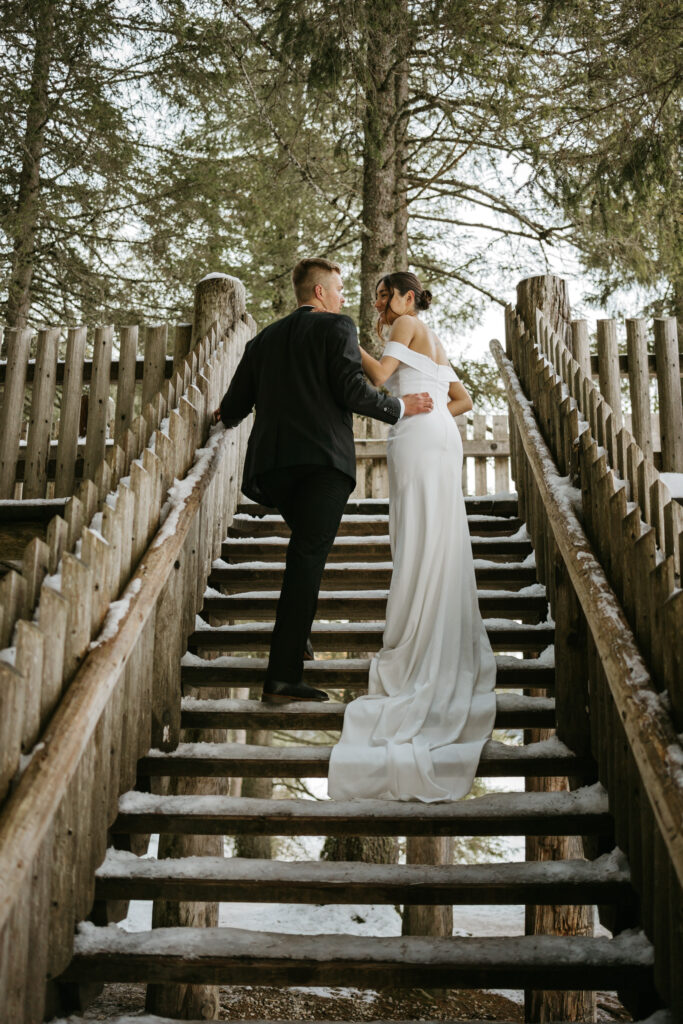 Bride and groom ascending wooden staircase outdoors.