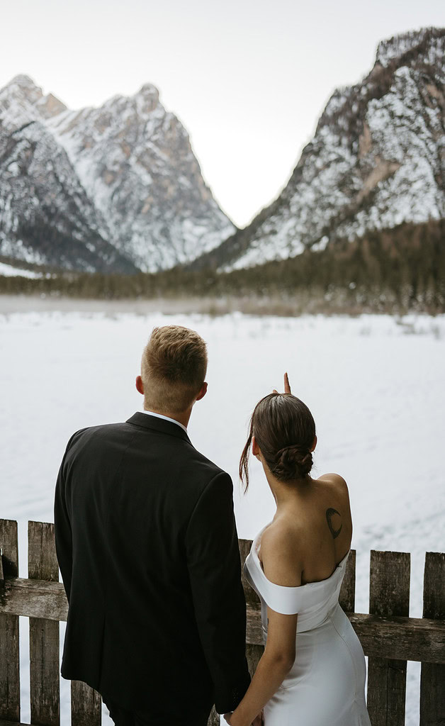 Couple in formal attire admires snowy mountains.