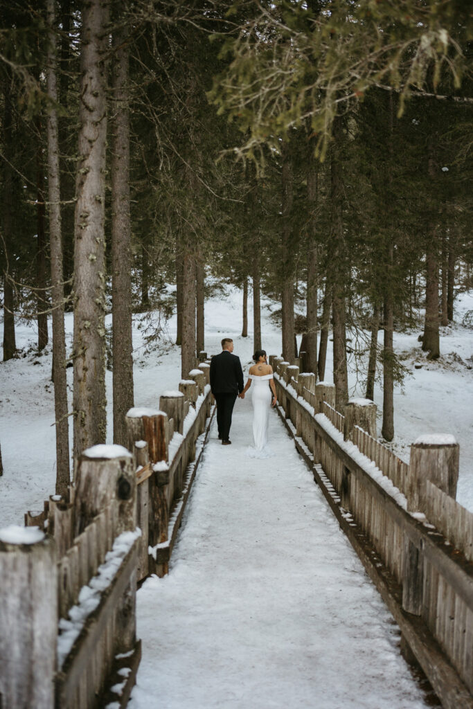 Couple walking on snowy bridge in forest.