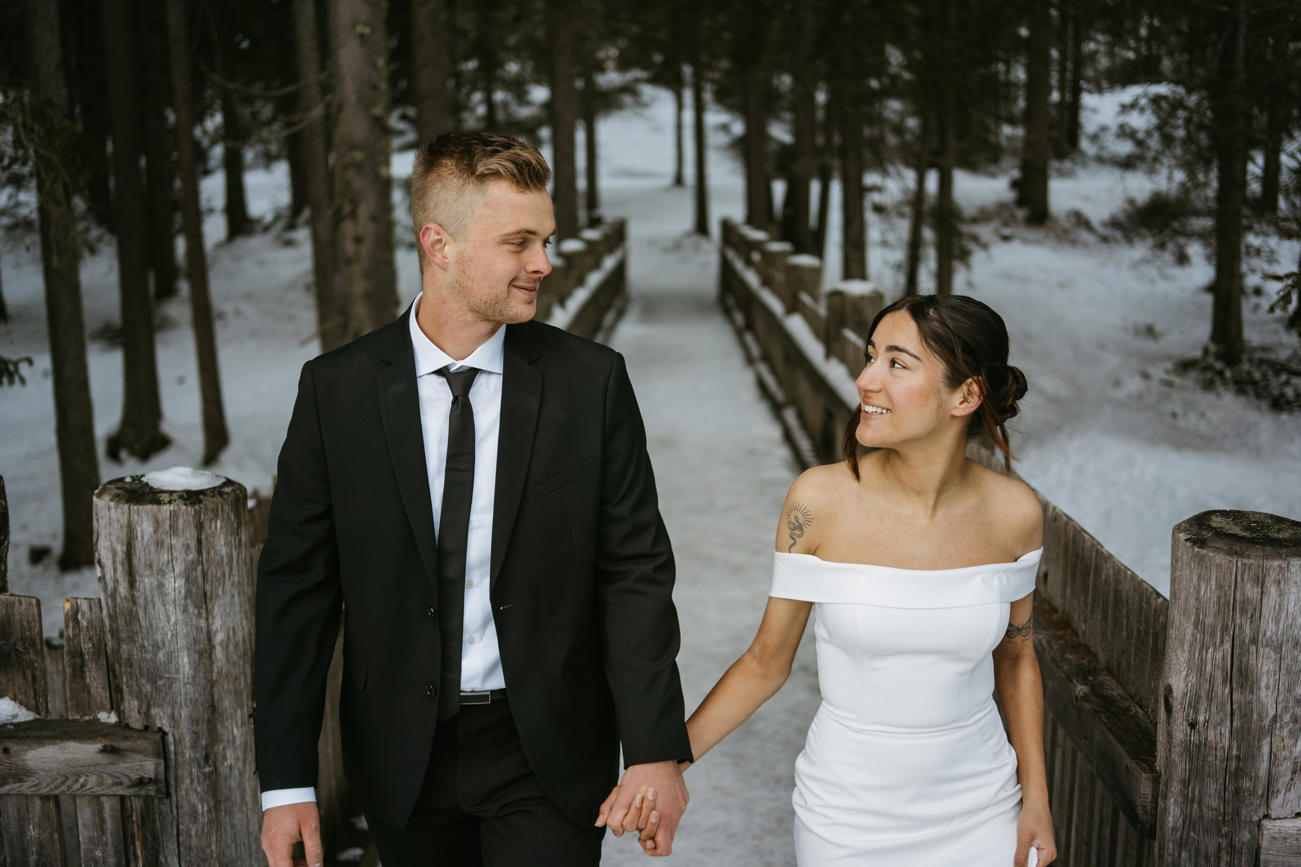 Couple holding hands on snowy wooden bridge.