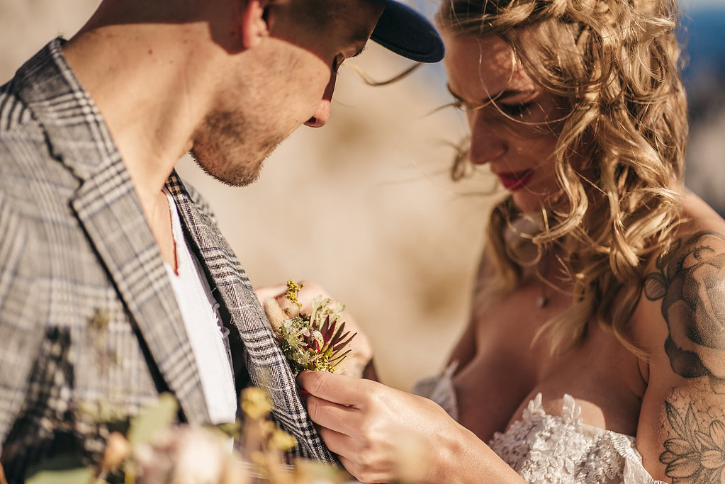 Couple adjusting boutonniere at wedding ceremony.