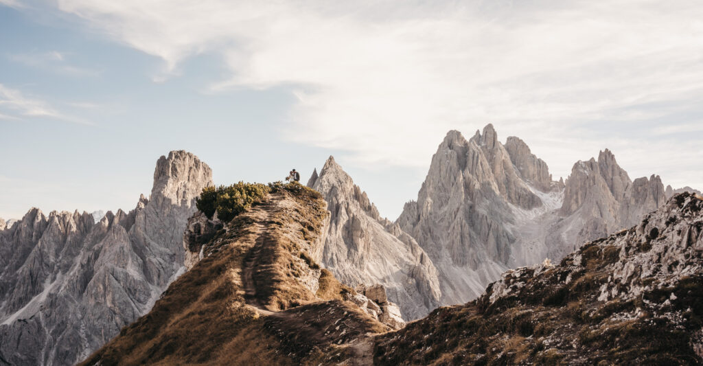 Couple on mountain ridge with jagged peaks.