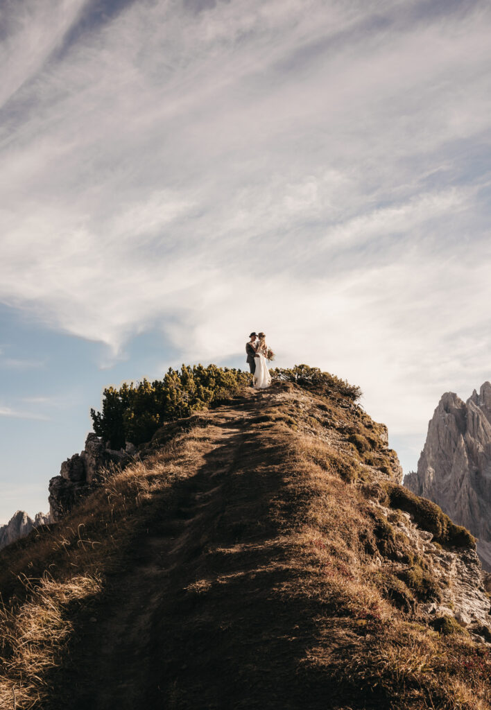 Couple standing on mountain peak under cloudy sky.