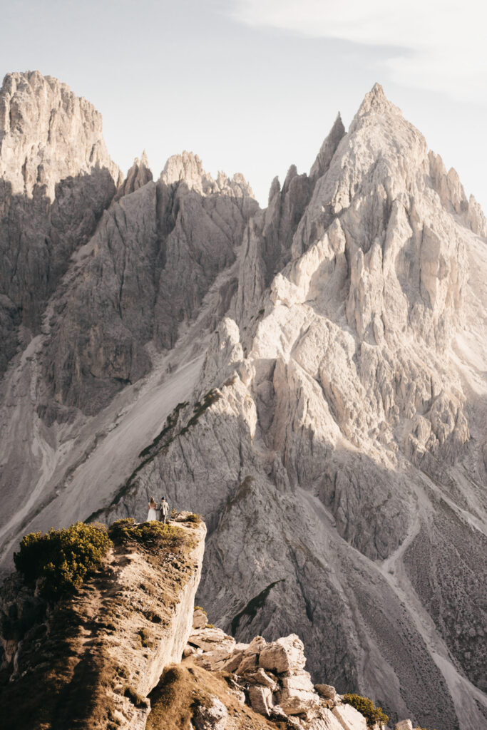 Couple stands on mountain cliff with scenic peaks.