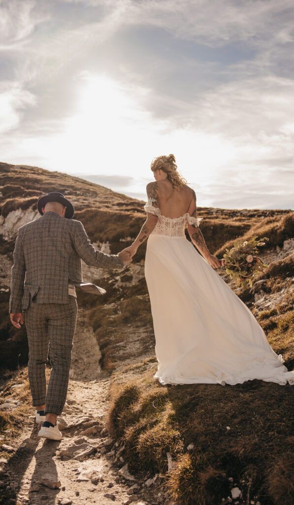 Couple holding hands on hill during wedding photoshoot.