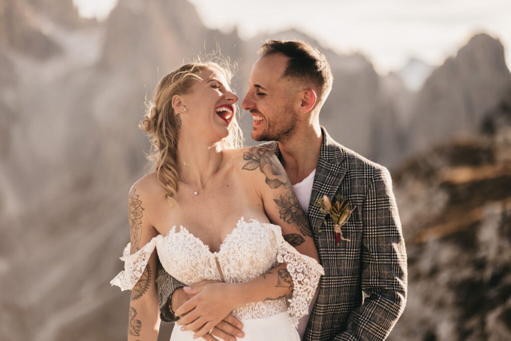 Happy couple laughing outdoors in wedding attire.