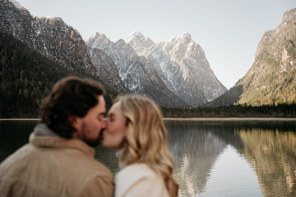 Couple kissing by a serene mountain lake.