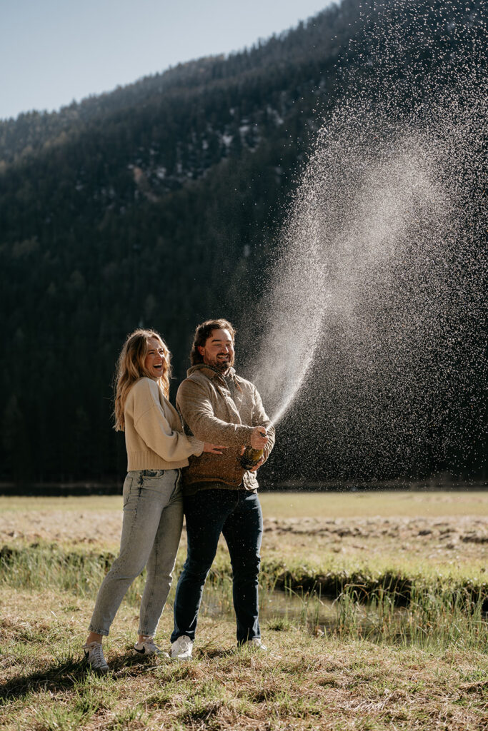 Couple celebrating with champagne in mountain meadow.