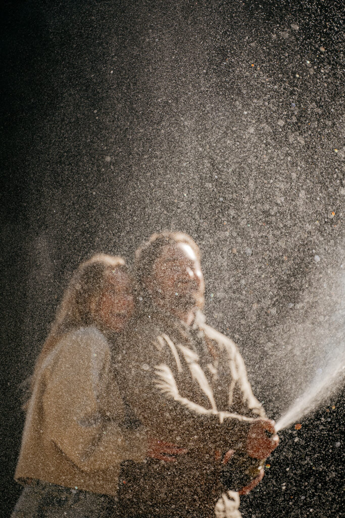 Couple celebrating with champagne spray in sunlight.