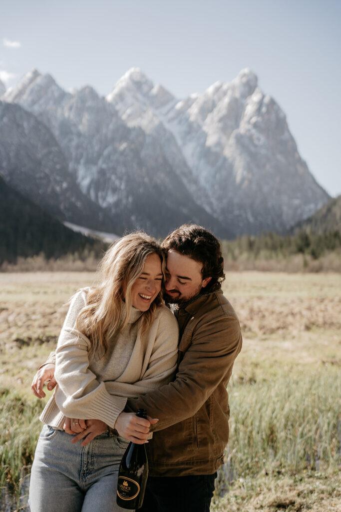 Couple outdoors with mountain view and wine bottle.