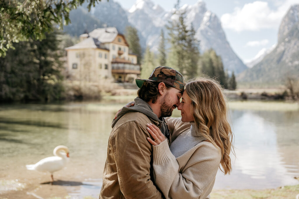 Couple embracing by lake with mountains and swan.