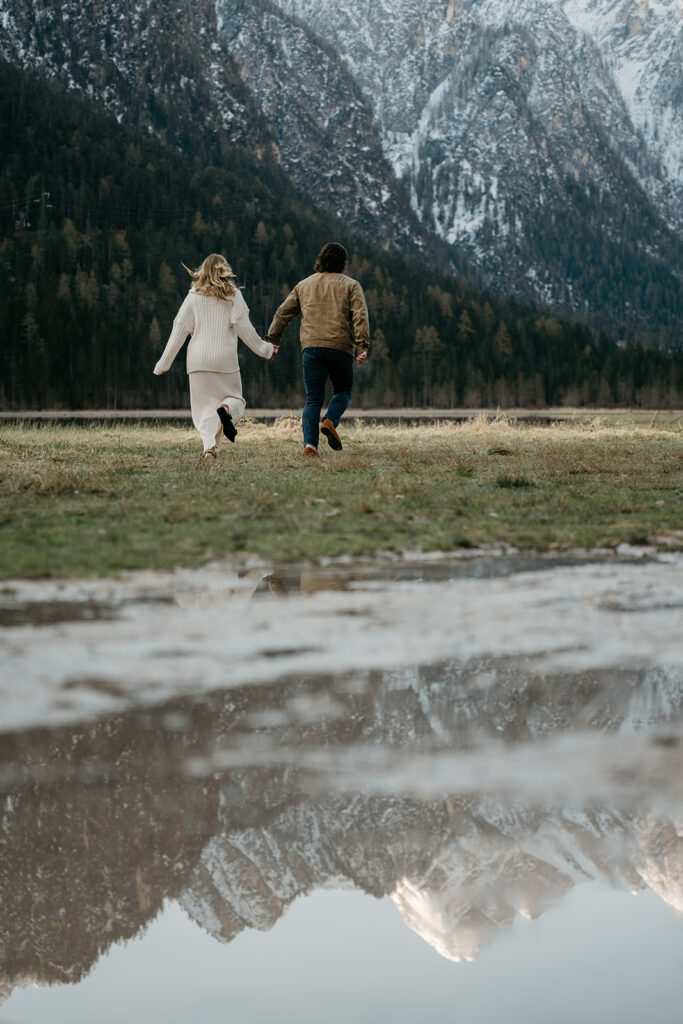 Couple running toward snowy mountains reflection in water.