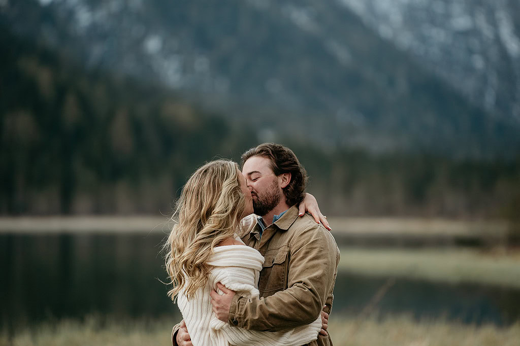 Couple kissing by a scenic mountain lake.