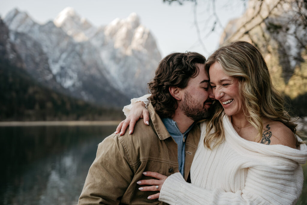 Couple embracing by a lake with mountains.