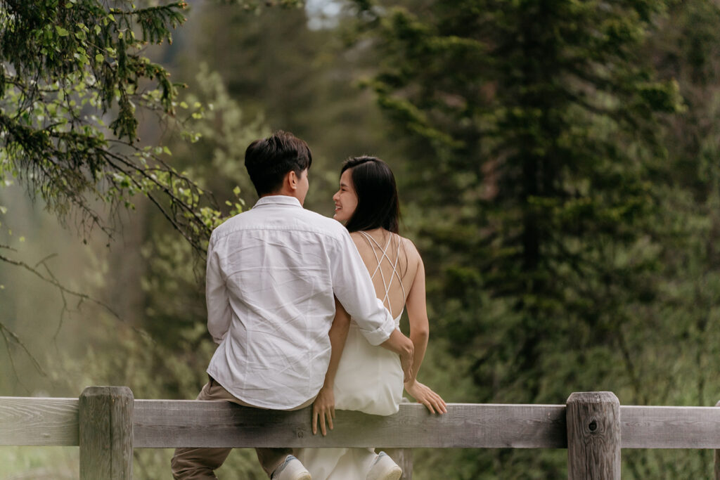 Couple sitting on a wooden fence in forest.