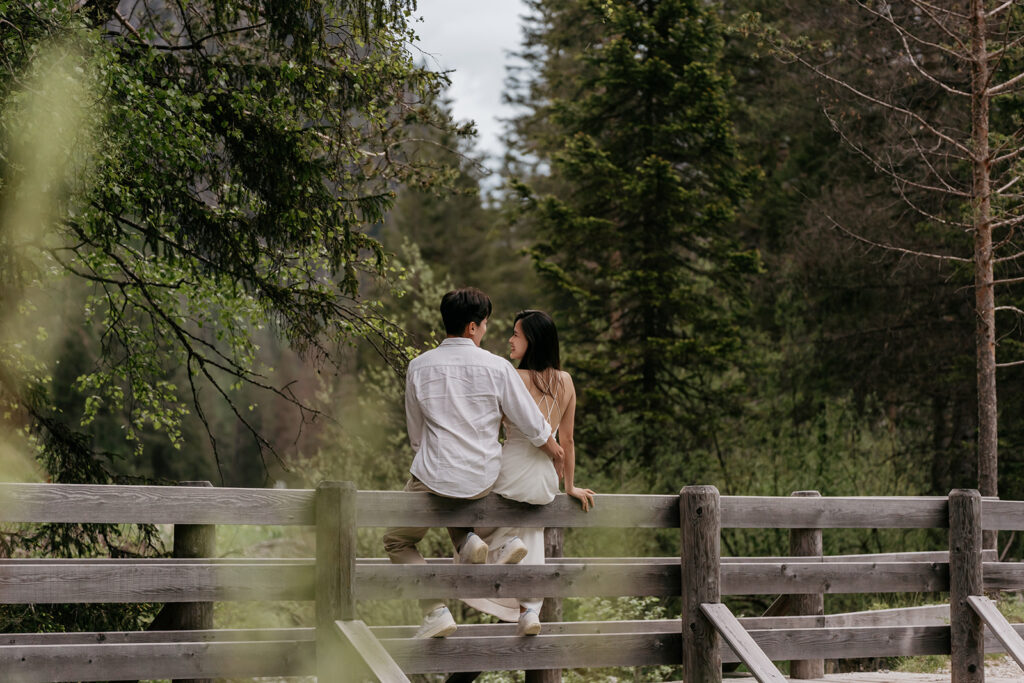 Couple sitting on wooden fence in forest