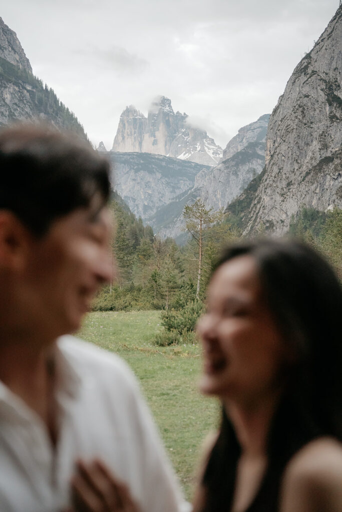 Two people laughing near scenic mountains.