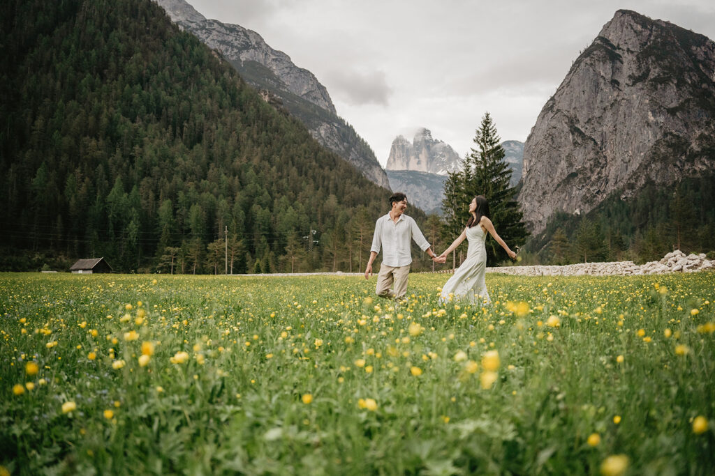 Couple walking in mountain field with flowers.