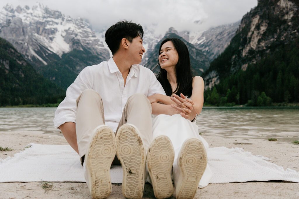 Couple sitting by a lake with mountains.