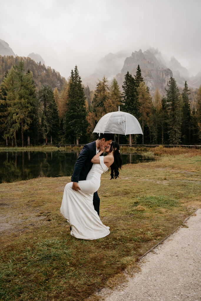 Couple kissing under umbrella in forest setting.