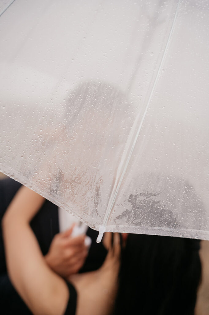 Couple embracing under a raindrop-covered umbrella.