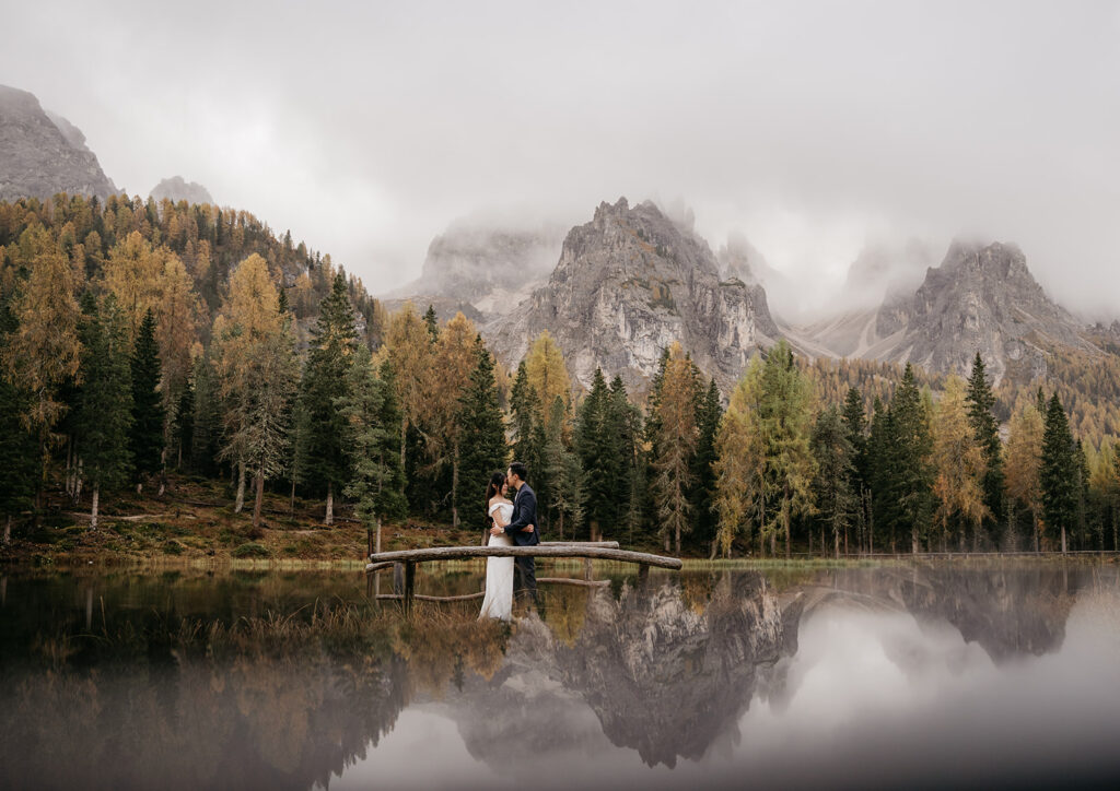 Couple kissing on bridge in forested mountains.