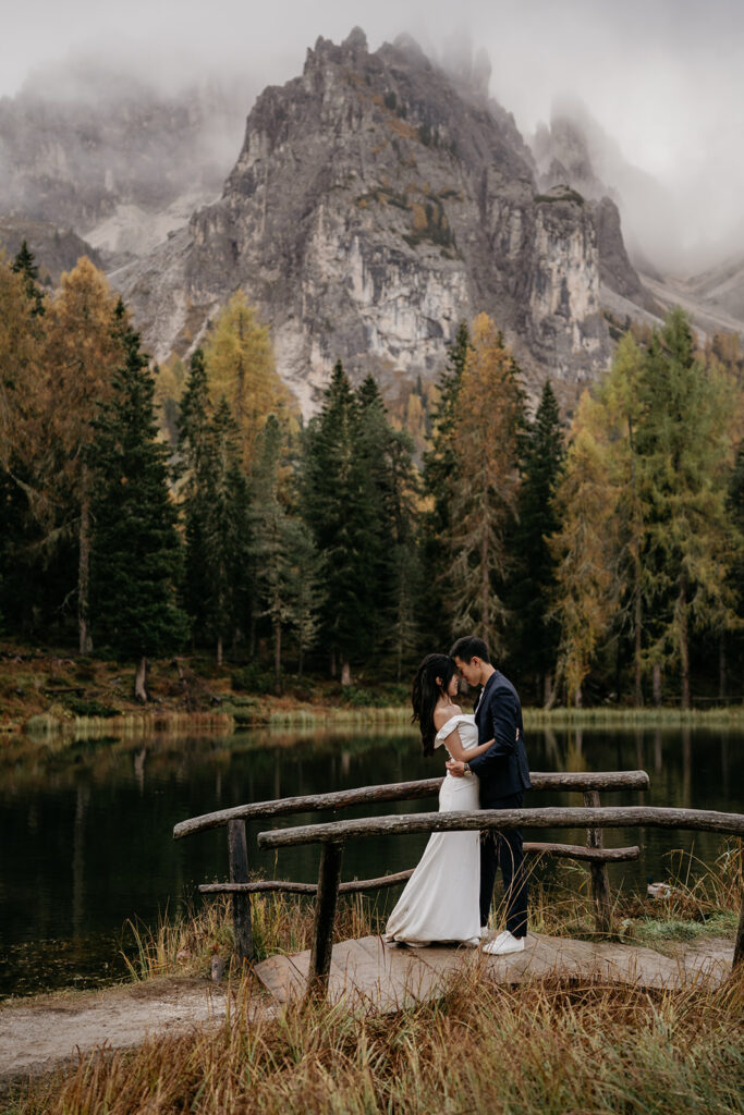 Couple embracing by mountain lake with trees.