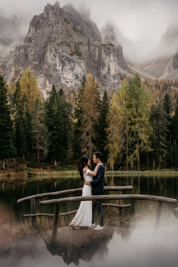 Couple embraces by lake with mountains in background.