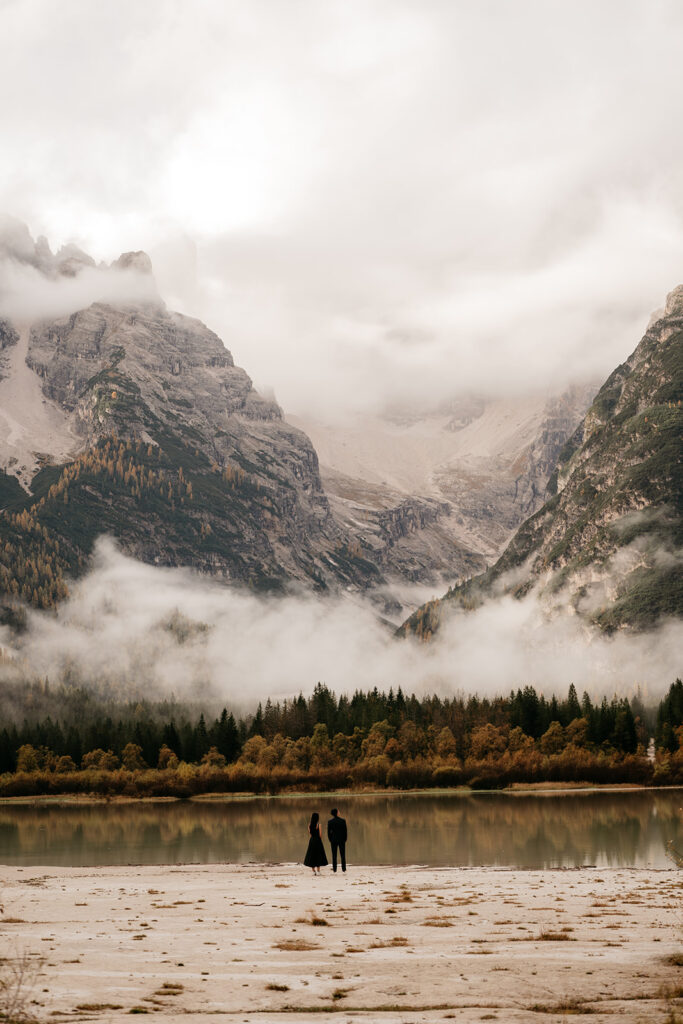 Couple standing by misty mountain lake landscape.