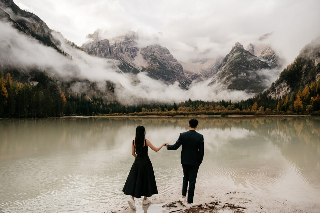 Couple holding hands by misty mountain lake.