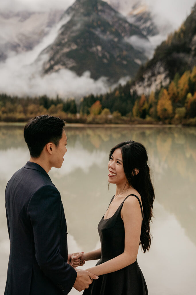 Couple smiling by a serene mountain lake.