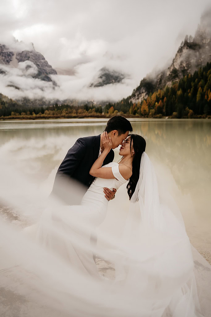 Bride and groom kissing by a misty lake