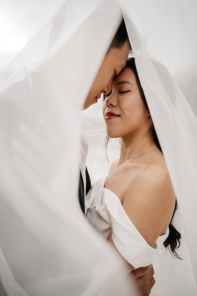 Couple embracing under flowing wedding veil.