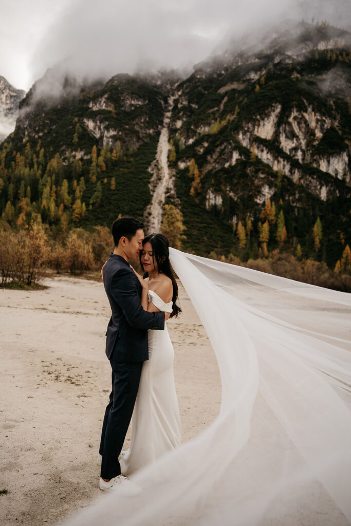 Bride and groom embrace in mountainous landscape.